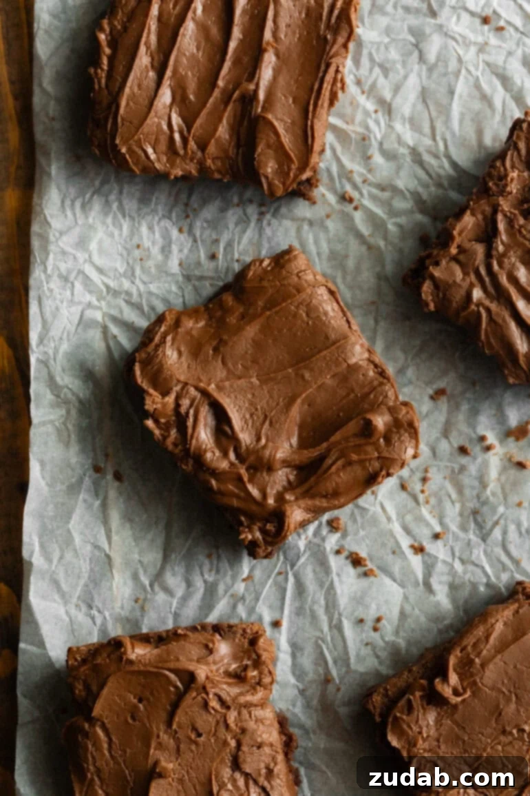 Classic Cafeteria Frosted Brownies 4 A freshly baked pan of thick, fudgy chocolate brownies with rich, glossy chocolate frosting, cooling on parchment paper, ready to be cut into squares.