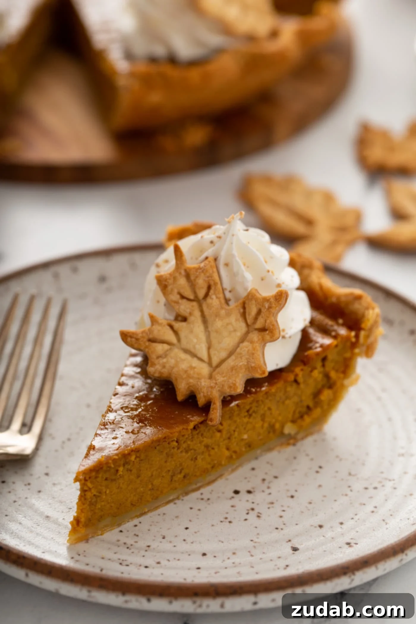 Pure Pumpkin Pie: Easy Homemade Bliss 3 A single slice of pumpkin pie topped with piped whipped cream and a pie crust leaf.