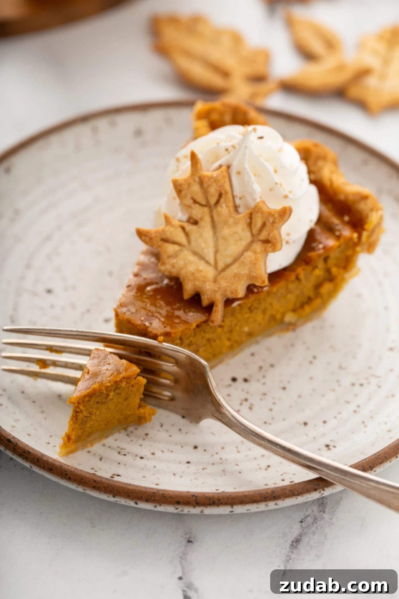 Pure Pumpkin Pie: Easy Homemade Bliss 7 A photo of a slice of pumpking pie with a fork slicing through the end topped with piped whipped cream and a pie crust leaf.