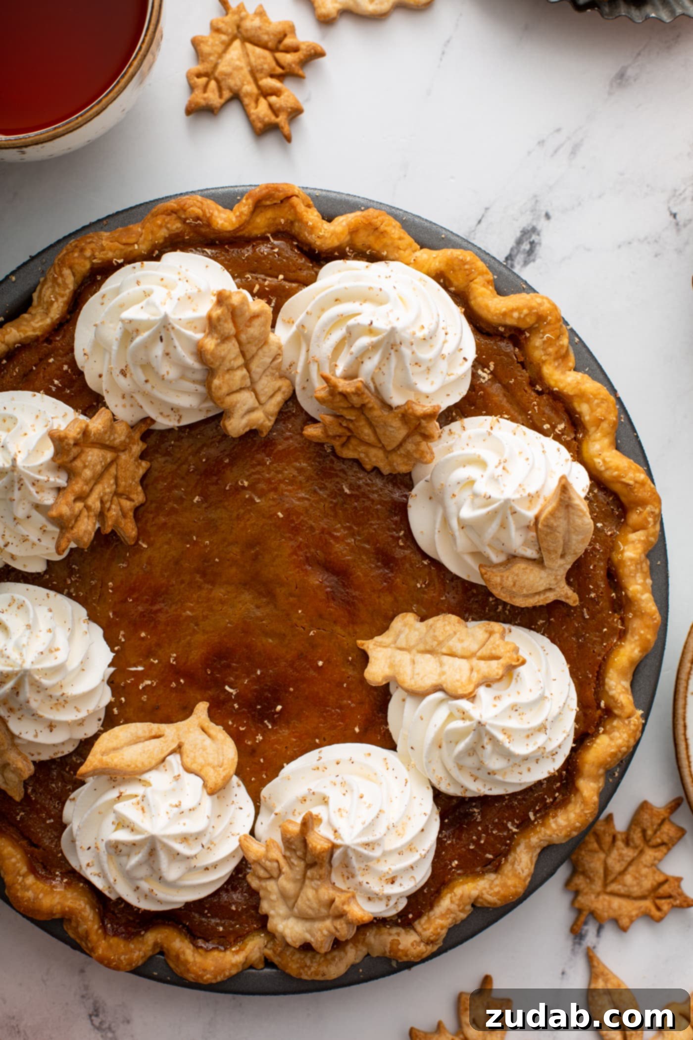 Pure Pumpkin Pie: Easy Homemade Bliss 10 A photo of a pumpkin pie topped with piped whipped cream and stamped pie crust leaves taken from above.
