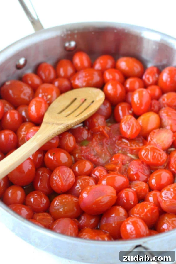 This 20 Minute Cherry Tomato and Basil Angel Hair Pasta comes together in a jiffy, and will satisfy the whole family, even the kids! grape tomatoes cooking in a pan with a wooden slotted spoon