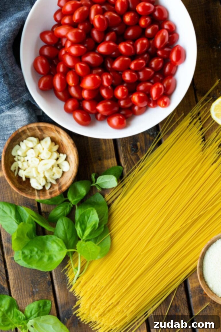 Quick and Easy 20-Minute Tomato Basil Angel Hair Pasta 4 a photo of a handful of uncooked angel hair pasta noodles, a bowl of cherry tomatoes, a bunch of fresh basil leaves and a small bowl of slice garlic cloves.