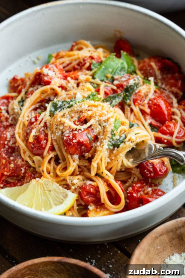 Quick and Easy 20-Minute Tomato Basil Angel Hair Pasta 8 a photo of a bowl full of angel hair pasta tossed with cooked grape tomatoes, fresh basil, granulated parmesan cheese and a slice of lemon.