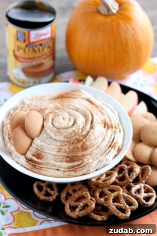 Delicious No-Bake Pumpkin Dip for Fall Gatherings Pumpkin Dip in a white bowl surrounded by pretzels, wafers and sliced apples.