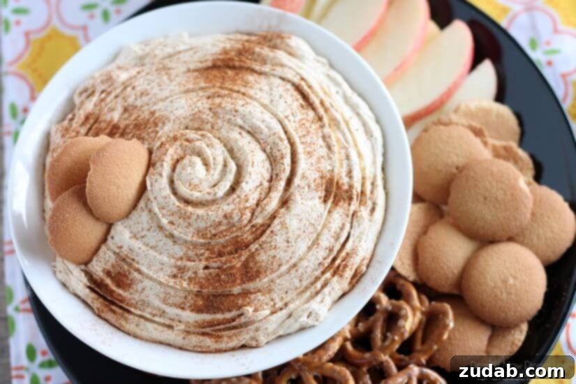 Creamy Pumpkin Cheesecake Dip with Fruit and Cookies pumpkin cream cheese Dip surrounded by pretzels, wafers and sliced red apples on a black plate.