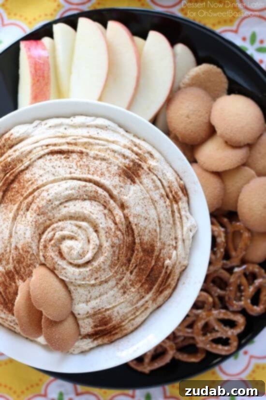 Versatile Pumpkin Dip Serving Ideas Pumpkin Dip in a white bowl on top of a black plate with pretzels, wafers and sliced apples.