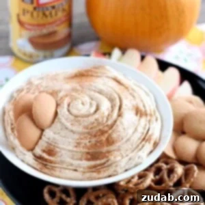 Spiced Pumpkin Cheesecake Indulgence 2 Pumpkin Cheesecake Dip in a white bowl surrounded by pretzels, wafers and sliced apples.