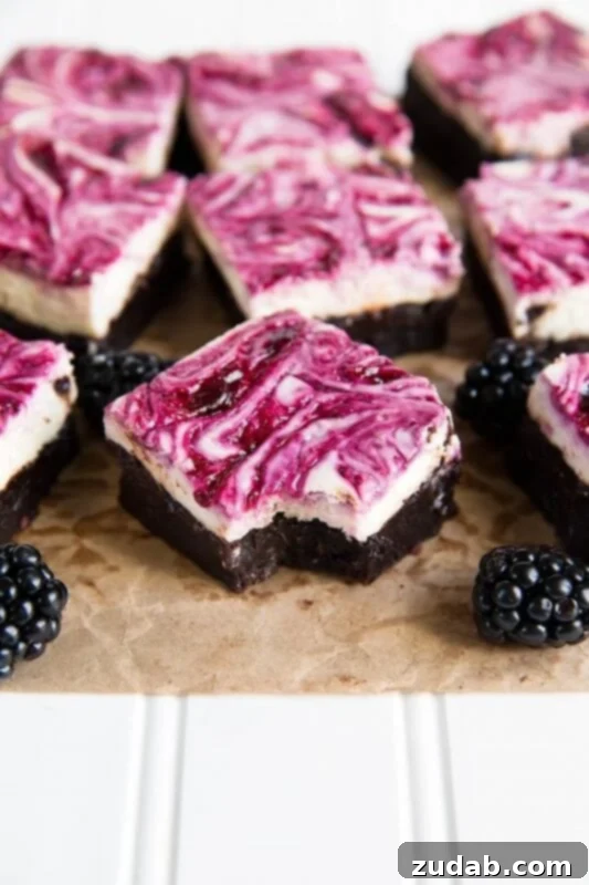 Irresistible Blackberry Cheesecake Brownies: A Rich Brownie Base, Tangy Cheesecake, and Sweet Blackberry Swirl! A photo of several square fudgy brownies topped with a cheesecake layer swirled with blackberry puree with whole blackberries scattered around the brownies, highlighting their gourmet appearance and delicious layers.