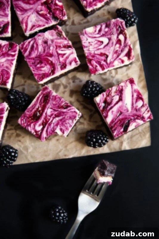 Decadent Swirl: Blackberry Cheesecake Brownies for an Unforgettable Treat A photo taken over the top of square brownies scattered on a brown piece of parchment with blackberry cheesecake swirled on top and whole blackberries scattered around the brownies, emphasizing the beautiful swirl.