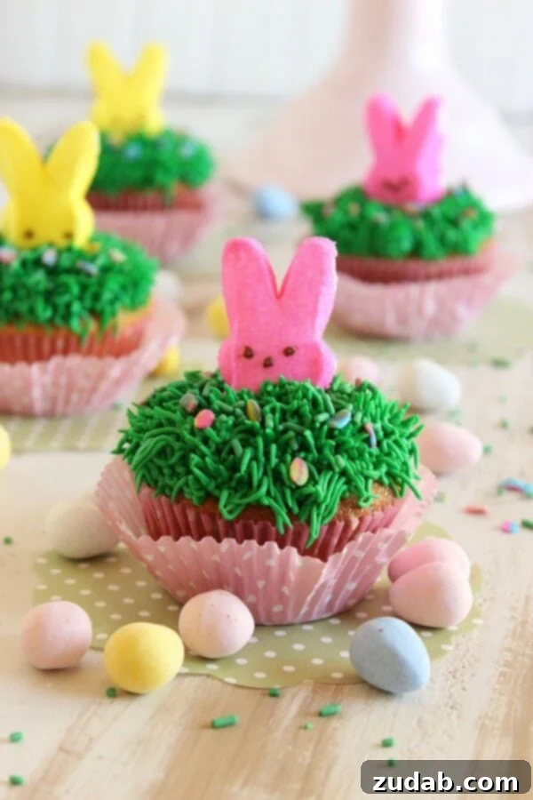 Easter Bunny Cadbury Mini Egg Cupcakes A close-up of a beautifully decorated Cadbury Mini Egg Cupcake with a bunny Peep peeking through green frosting grass, ideal for an Easter dessert.