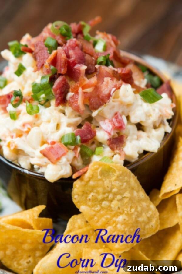 Bacon Ranch Corn Dip ohsweetbasil.com Close-up view of a chilled bacon ranch corn dip in a dark serving bowl, surrounded by crispy tortilla chips, highlighting its creamy texture and visible corn and bacon bits.