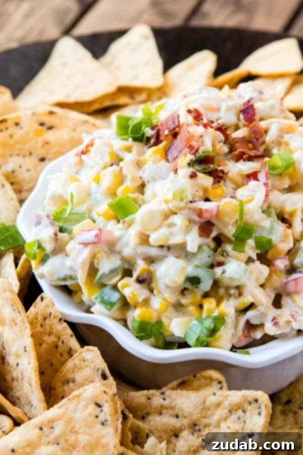 The Ultimate Cheesy Bacon Ranch Corn Dip 3 A close-up of a delightful corn and bacon ranch dip in a pristine white dish, adorned with fresh green onions and crispy bacon bits, ready for serving with crunchy tortilla chips.