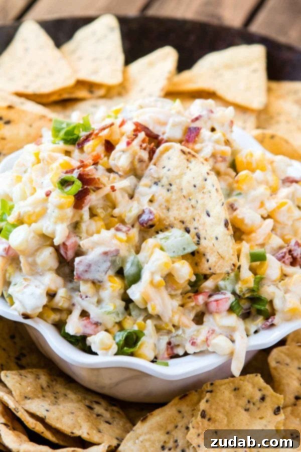 The Ultimate Cheesy Bacon Ranch Corn Dip 4 A vibrant and cheesy corn dip presented in a white ceramic bowl, encircled by a generous scattering of golden tortilla chips, highlighting its festive and inviting nature.