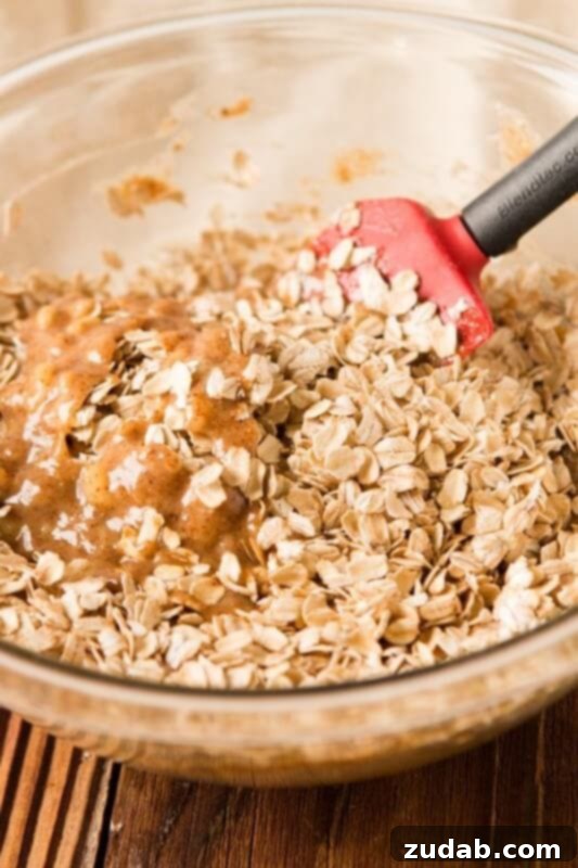 Spiced White Chocolate Cranberry Breakfast Cookies 7 A clear glass bowl filled with the textured oatmeal breakfast cookie dough, being mixed with a spatula.