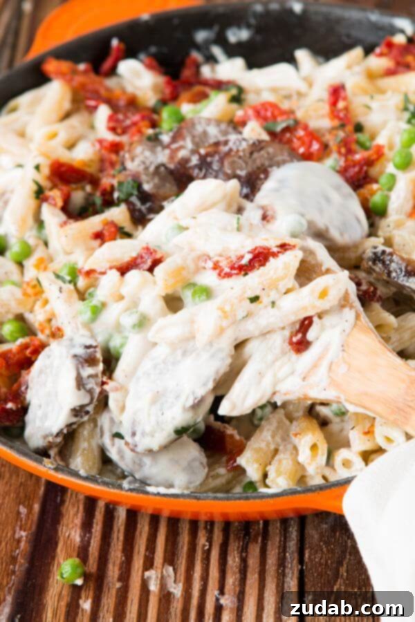 Quick and Easy Sausage Alfredo Pasta for Dinner Overhead view of a serving of easy sausage Alfredo pasta, garnished with fresh green peas and chopped parsley, ready to be enjoyed