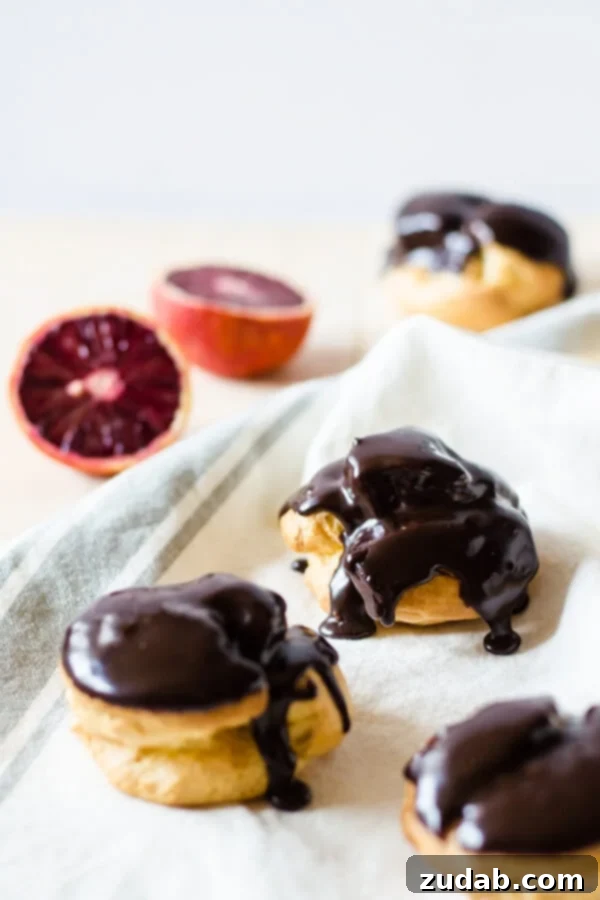 Delicate choux pastry puffs generously filled with a velvety blood orange cream and drizzled with a rich chocolate ganache, creating an exquisite dessert.