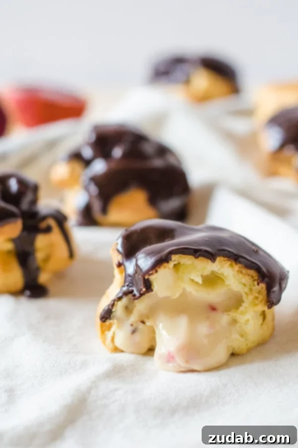 Close-up of a perfectly baked cream puff, sliced open to reveal its luscious blood orange pastry cream filling and a decadent chocolate ganache topping.