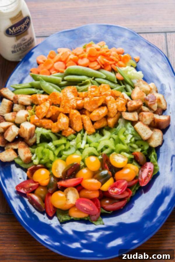 Delicious Buffalo Chicken Salad with Blue Cheese Dressing A close-up of a vibrant Buffalo Chicken Salad with crisp lettuce, carrots, celery, sugar snap peas, tomatoes, topped with spicy buffalo chicken and a drizzle of creamy blue cheese dressing, garnished with golden croutons.