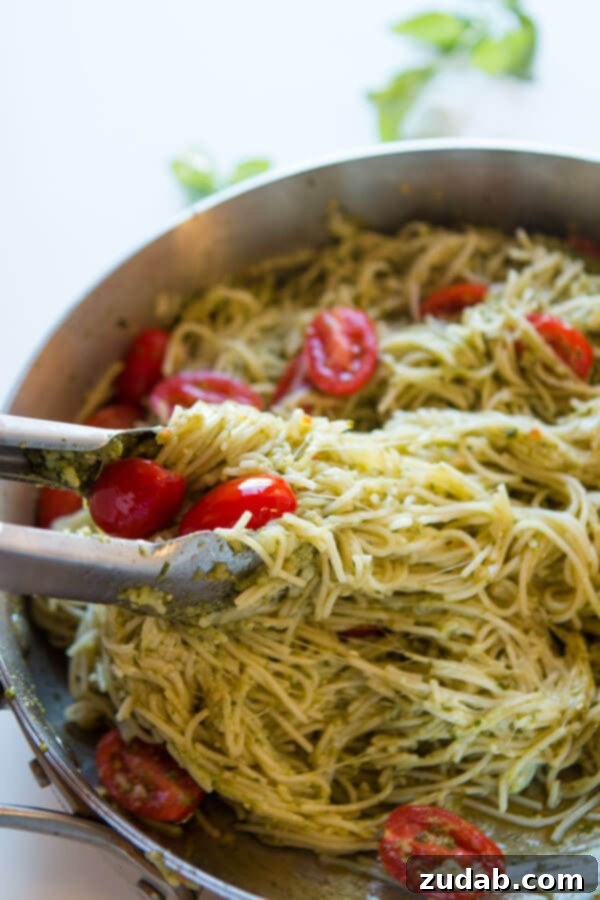 Need dinner on the table in 20 minutes? We've got a 20 minute cheesy pesto pasta recipe that's quick and easy to make and it's a great special diets recipe. Tongs gracefully lifting a generous tangle of basil pesto pasta from a hot skillet, showcasing the perfectly coated noodles and melted cheese, ready for serving.