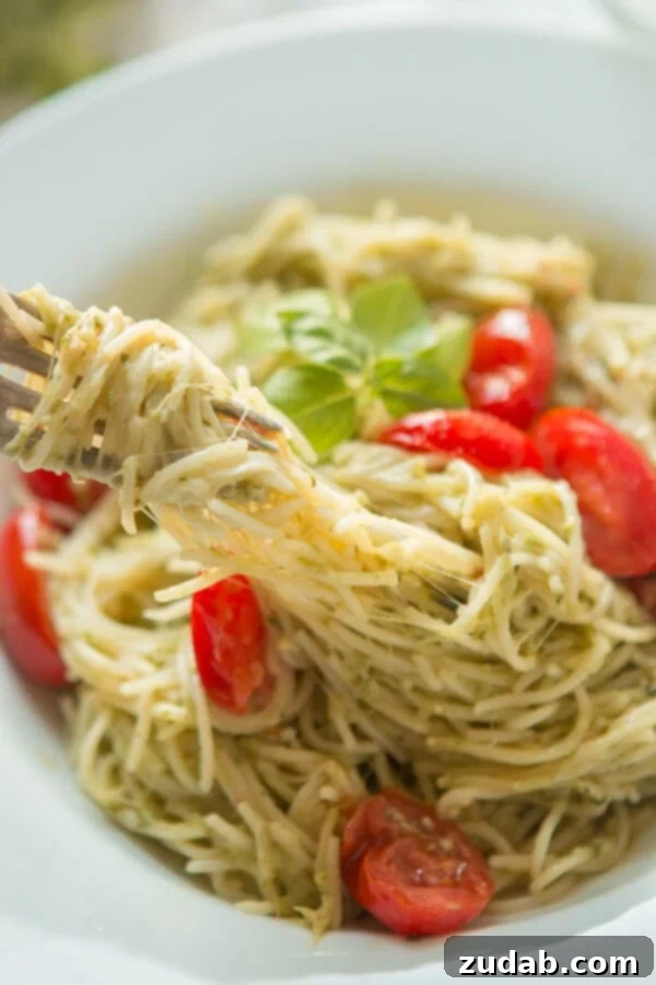 Need dinner on the table in 20 minutes? We've got a 20 minute cheesy pesto pasta recipe that's quick and easy to make and it's a great special diets recipe. A close-up shot of a fork twirling a generous portion of cheesy pesto pasta from a white bowl, highlighting the rich green sauce, melted cheese, and tender noodles, ready to be enjoyed.