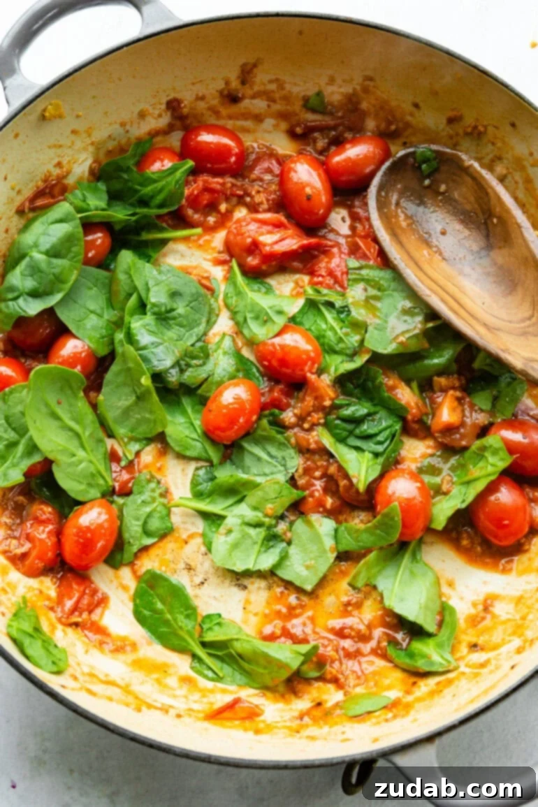 Quick Cheesy Pesto Pasta 6 A step-by-step photo gallery capturing the cooking process: first, garlic and grape tomatoes sizzling in olive oil, followed by spinach and fresh basil leaves being added, creating a flavorful base for the pesto pasta.