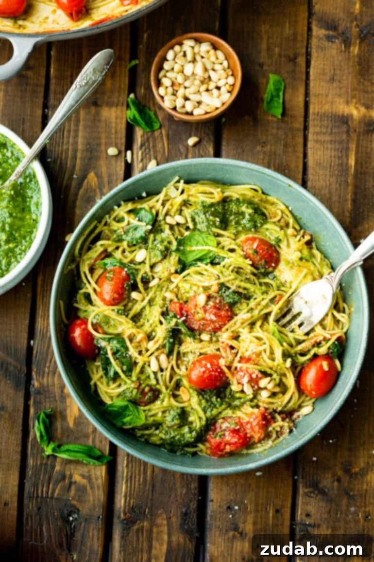 Quick Cheesy Pesto Pasta 8 A large bowl of vibrant green pesto pasta is artfully arranged next to a small bowl of fresh pesto and another bowl of golden toasted pine nuts, highlighting the key components of the dish.