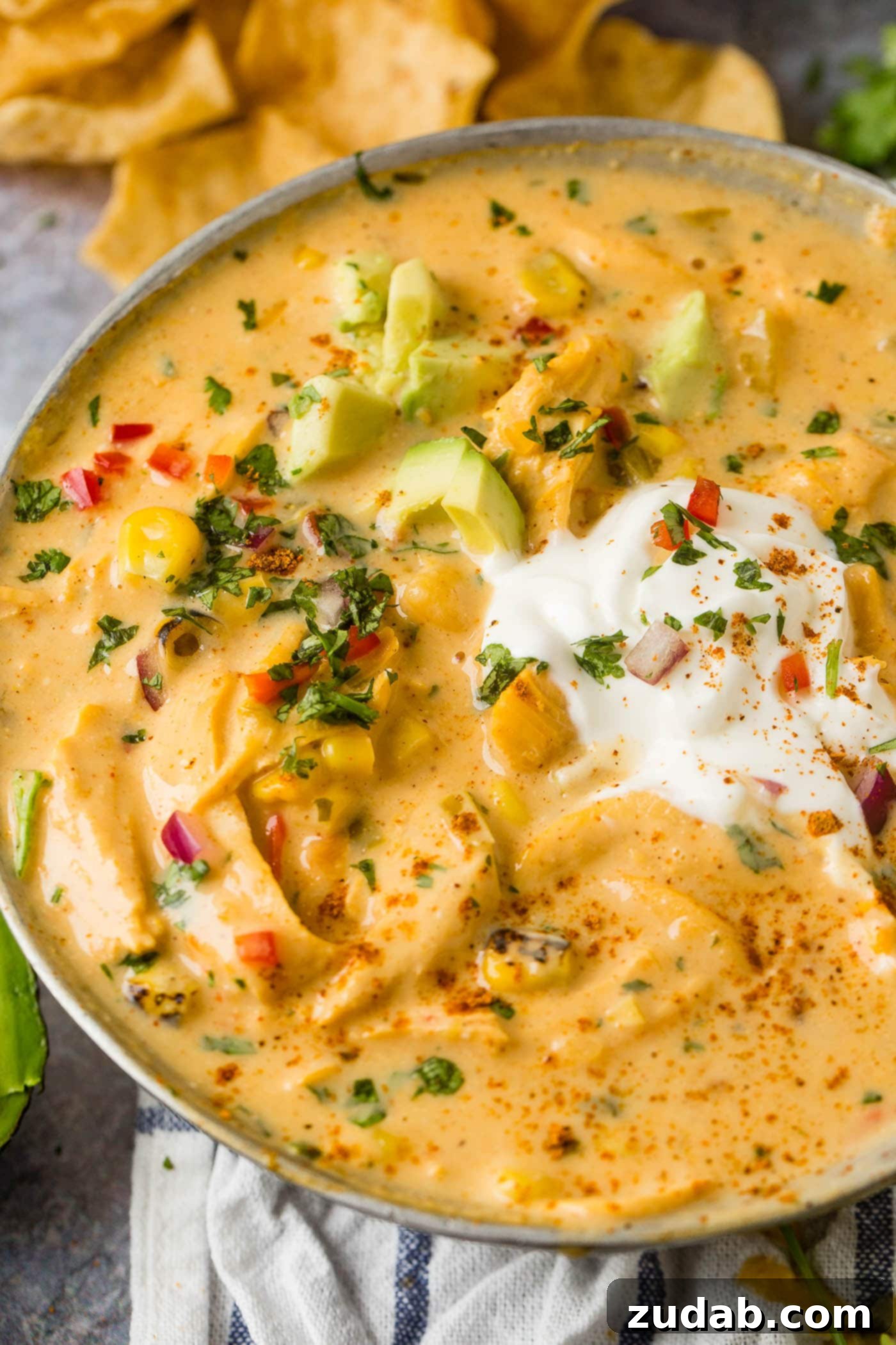 Hearty Cheesy Southwestern Chicken Tortilla Soup 5 A bowl of rich cheesy chicken tortilla soup, topped with fresh sour cream and slices of vibrant green avocado.