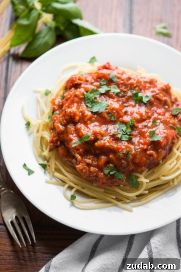 Unlock the secret to the most delicious homemade spaghetti sauce recipe – a timeless family favorite perfected over the years. Spaghetti topped with homemade pasta sauce, generously sprinkled with chopped parsley, served on a pristine white plate.