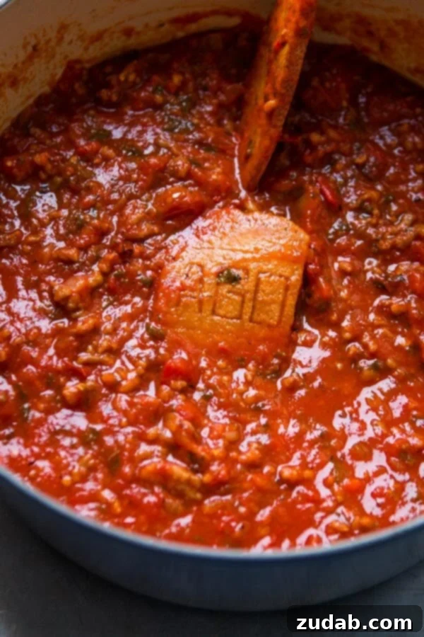 Discover the secret to the most delicious homemade spaghetti sauce recipe – a timeless family favorite perfected over the years. Homemade spaghetti sauce simmering gently in a vibrant blue Dutch oven, with the secret Parmesan rind slowly infusing its rich flavors.