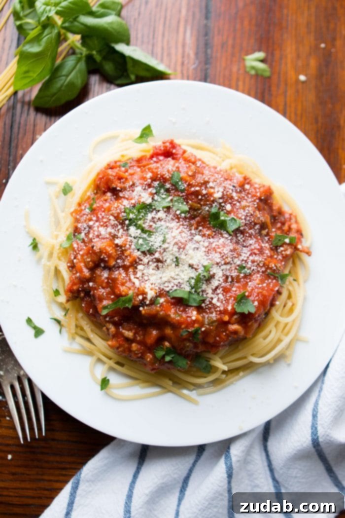 Discover the secret to the most delicious homemade spaghetti sauce recipe – a timeless family favorite perfected over the years. Perfectly cooked pasta topped with a generous serving of rich homemade spaghetti sauce and freshly grated Parmesan cheese on a pristine white plate.