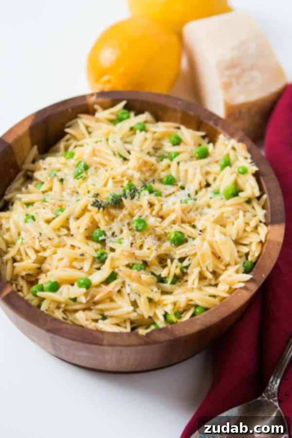 As the winter is starting to melt away we make recipes that scream spring like this Quick and easy lemon orzo with parmesan and peas. Homemade Quick and easy lemon orzo with parmesan and peas in small wooden bowl next to lemons and parmesan cheese.