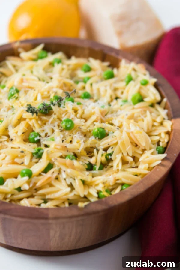 As the winter is starting to melt away we make recipes that scream spring like this Quick and easy lemon orzo with parmesan and peas. Wooden bowl of simple lemon orzo with parmesan and peas next to a red cloth.