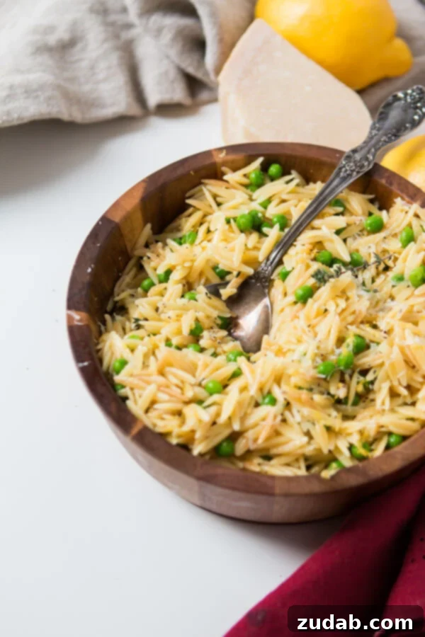 As the winter is starting to melt away we make recipes that scream spring like this Quick and easy lemon orzo with parmesan and peas. Silver spoon in a wooden bowl full of Quick and easy lemon orzo with parmesan and peas on a white table.