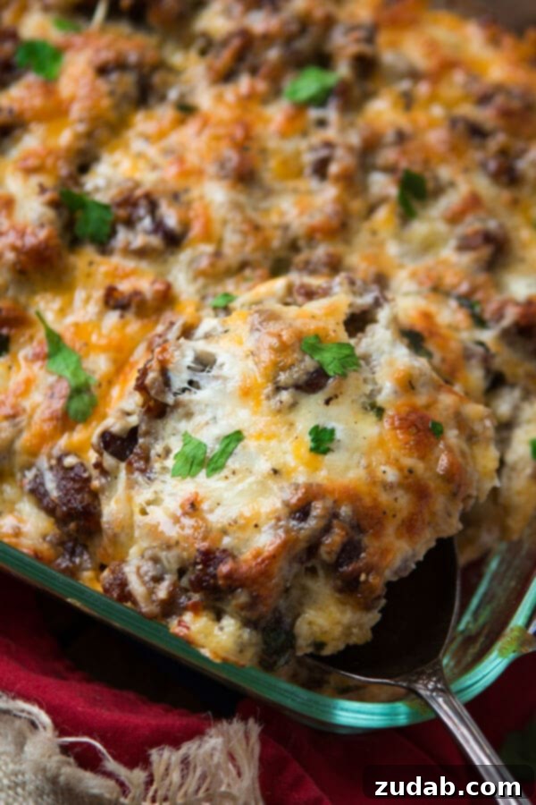 A serving spoon lifting a portion of cheesy hash brown sausage breakfast casserole from the baking dish, showcasing its golden-brown top and melted cheese. A serving spoon lifting a portion of cheesy hash brown sausage breakfast casserole from the baking dish, showcasing its golden-brown top and melted cheese.