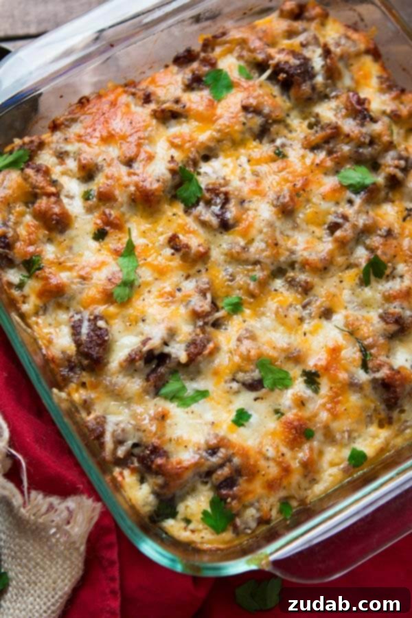Close-up of a cheesy hash brown sausage breakfast casserole in a square glass baking dish, showing the browned top and bubbly cheese. Close-up of a cheesy hash brown sausage breakfast casserole in a square glass baking dish, showing the browned top and bubbly cheese.