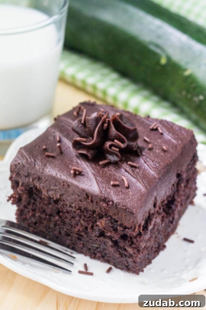 Decadent Double Chocolate Zucchini Cake 2 frosted chocolate zucchini cake slice on white plate next to glass of milk