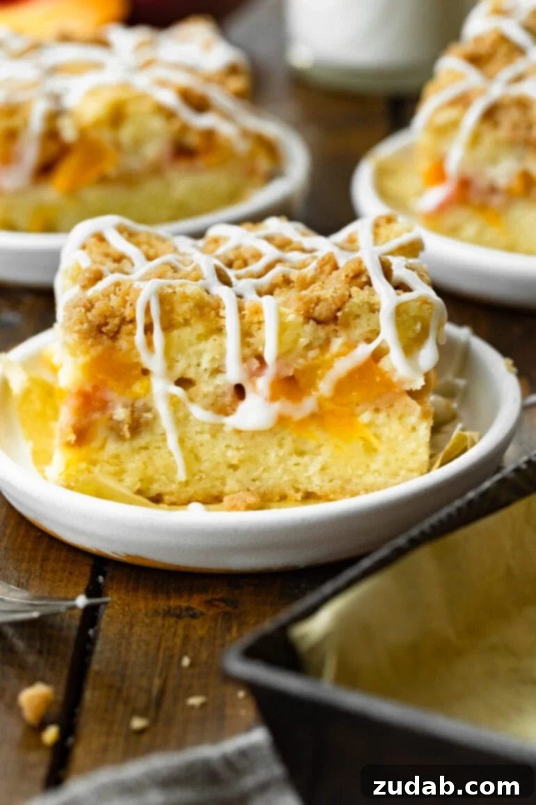 Peach Streusel Coffee Cake 2 a photo of a piece of peach coffee cake topped with a streusel topping and a creamy white drizzle.