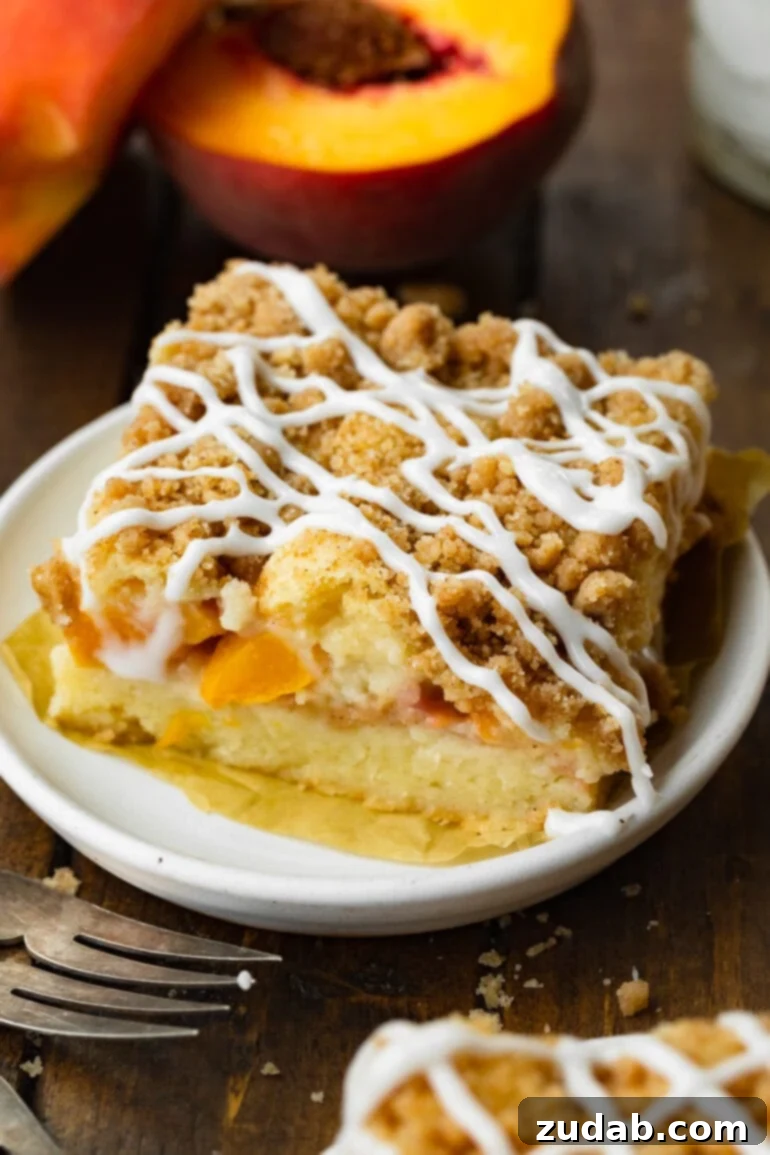 Peach Streusel Coffee Cake 4 a photo of a large piece of peach coffee cake sitting on a small dessert plate and topped with a crunchy cinnamon streusel topping and a vanilla glaze drizzled all over the top.