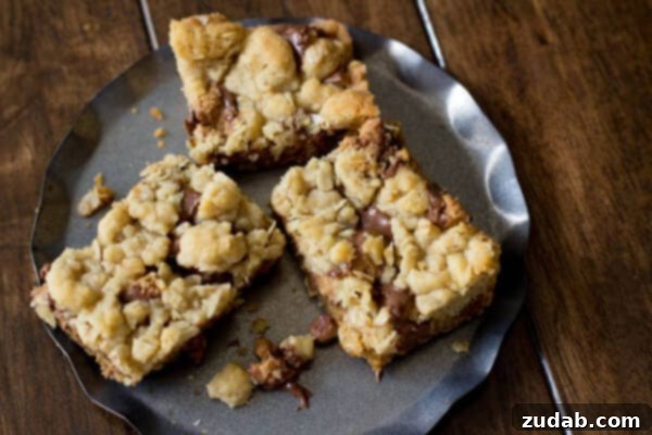 You will fall in love with these #Reeses Crumble bars. Buttery oatmeal cumble stuffed with chocolate chips and #Reesespeanutbuttercups ohsweetbasil.com_ Close-up of a single Reese's Crumble Bar on a wooden surface, showcasing the crumbly texture