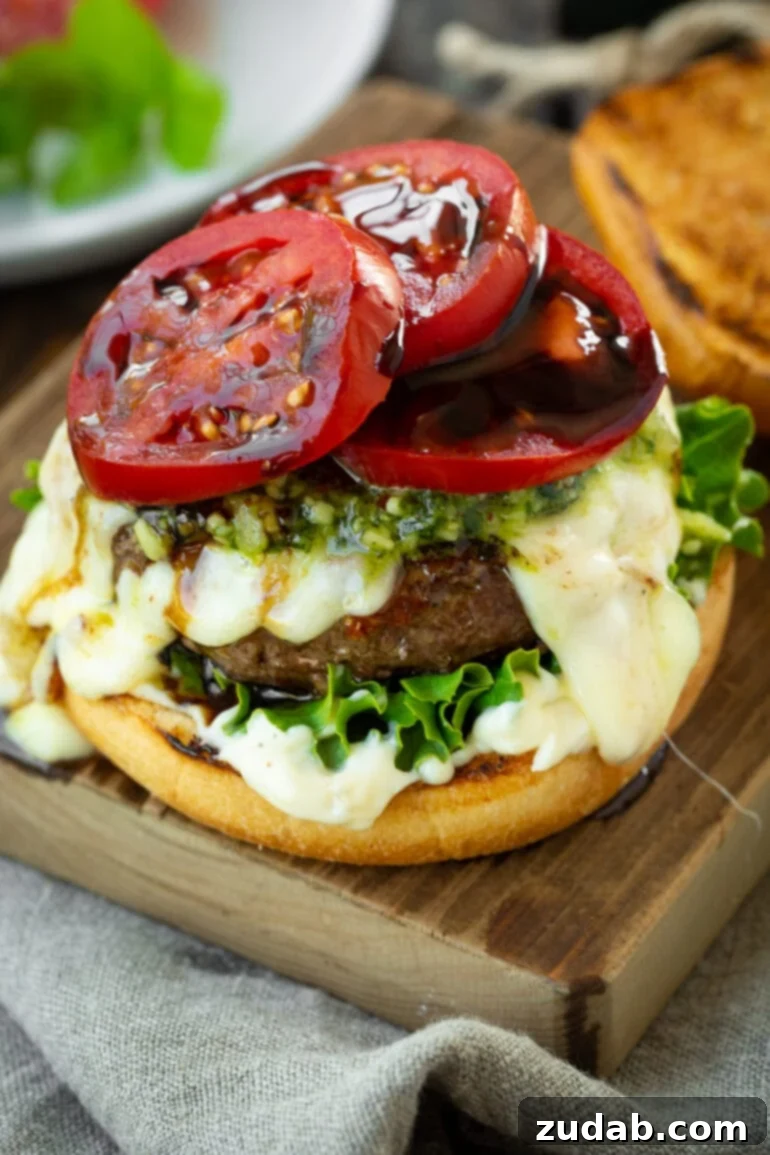 Aromatic Caprese Pesto Burgers 3 A close-up shot of a gourmet garlic pesto burger with the top bun removed, showcasing the vibrant tomato slices glistening with balsamic glaze, atop a bed of fresh lettuce, melted cheese, and a pesto-infused patty. An enticing view of burger perfection.