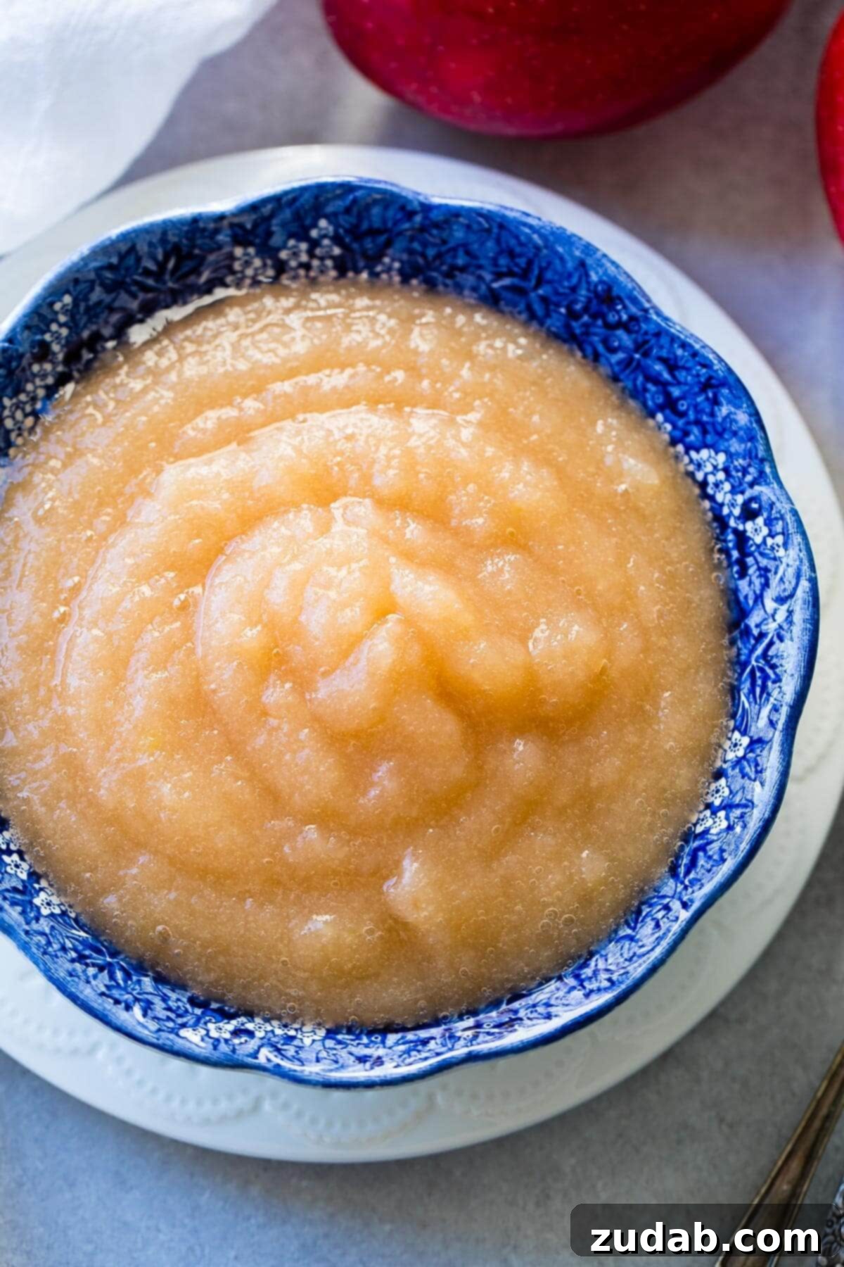 Easy 2-Ingredient Instant Pot Applesauce 3 Unsweetened homemade applesauce in a vibrant blue bowl on a white plate, ready to be enjoyed.