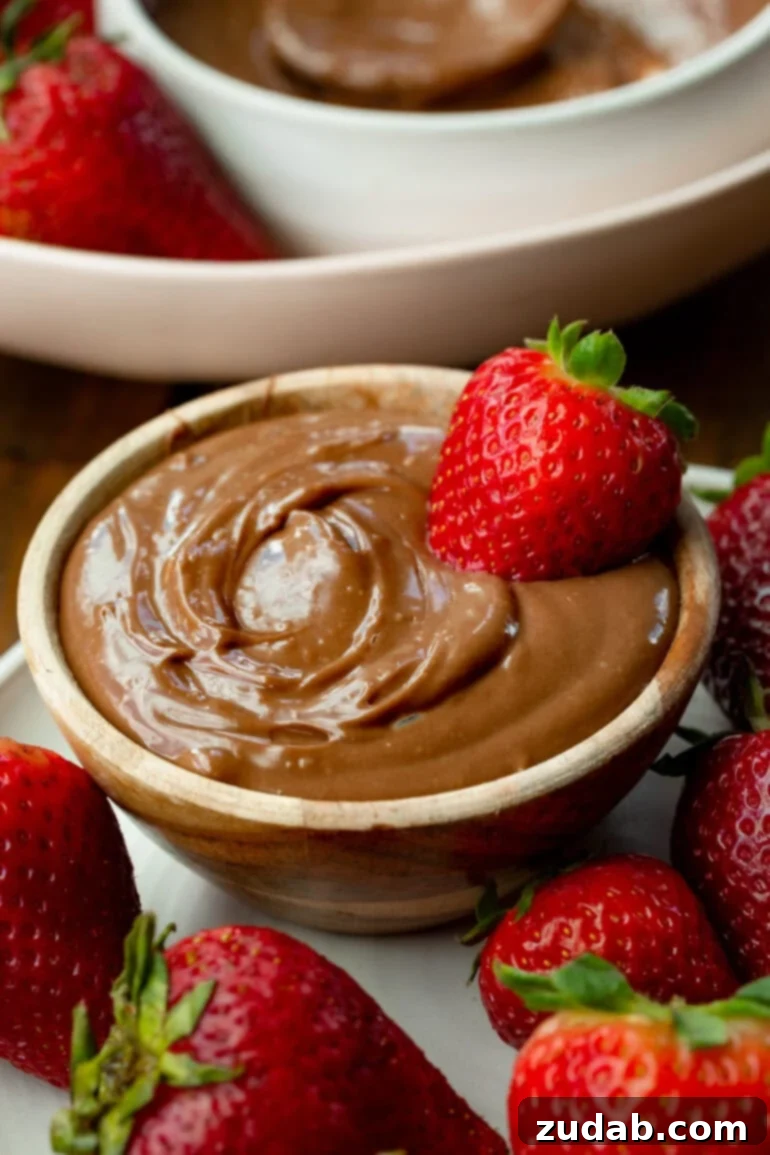 Guilt-Free Chocolate Strawberry Bliss 2 A small bowl filled with creamy chocolate yogurt dip with a whole strawberry dipped in it and strawberries scattered all around it, ready to be enjoyed as a healthy treat.
