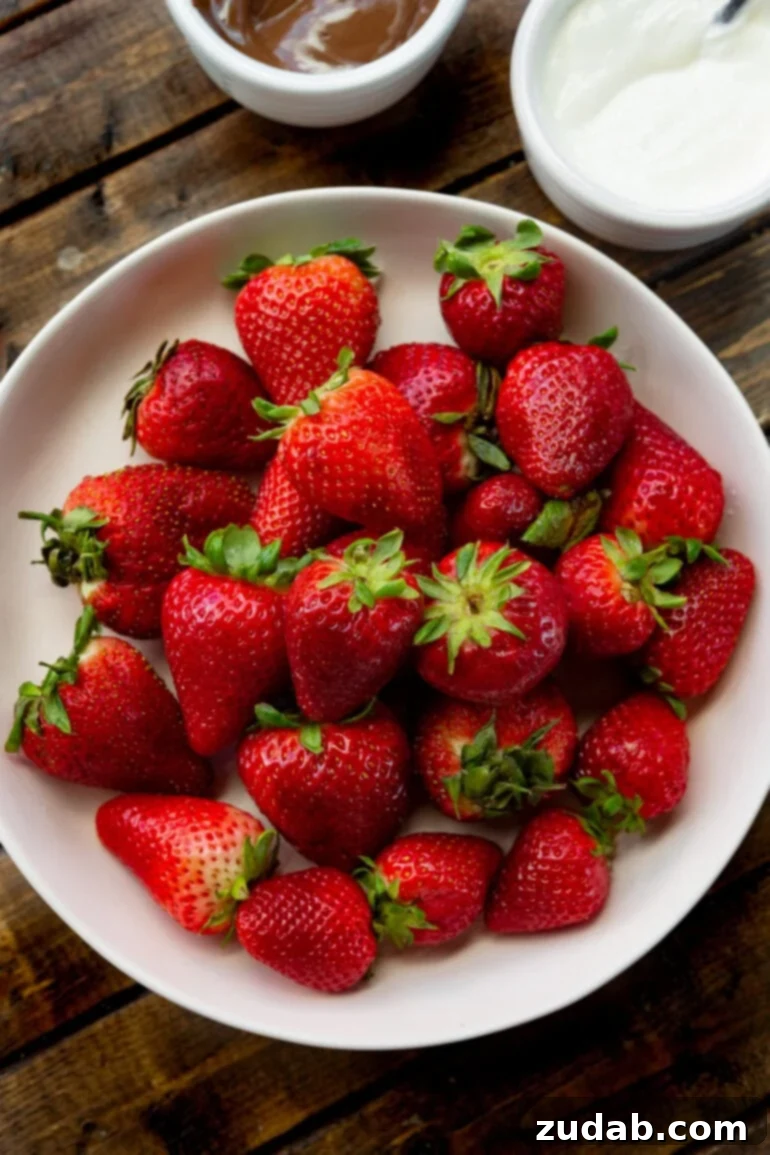 Guilt-Free Chocolate Strawberry Bliss 4 A large white plate overflowing with whole, bright red, ripe strawberries, ready for dipping in a healthy chocolate treat.