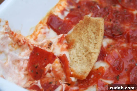 Ultimate Pepperoni Pizza Dip 3 a pita chip dunked into a baking dish of pepperoni pizza dip