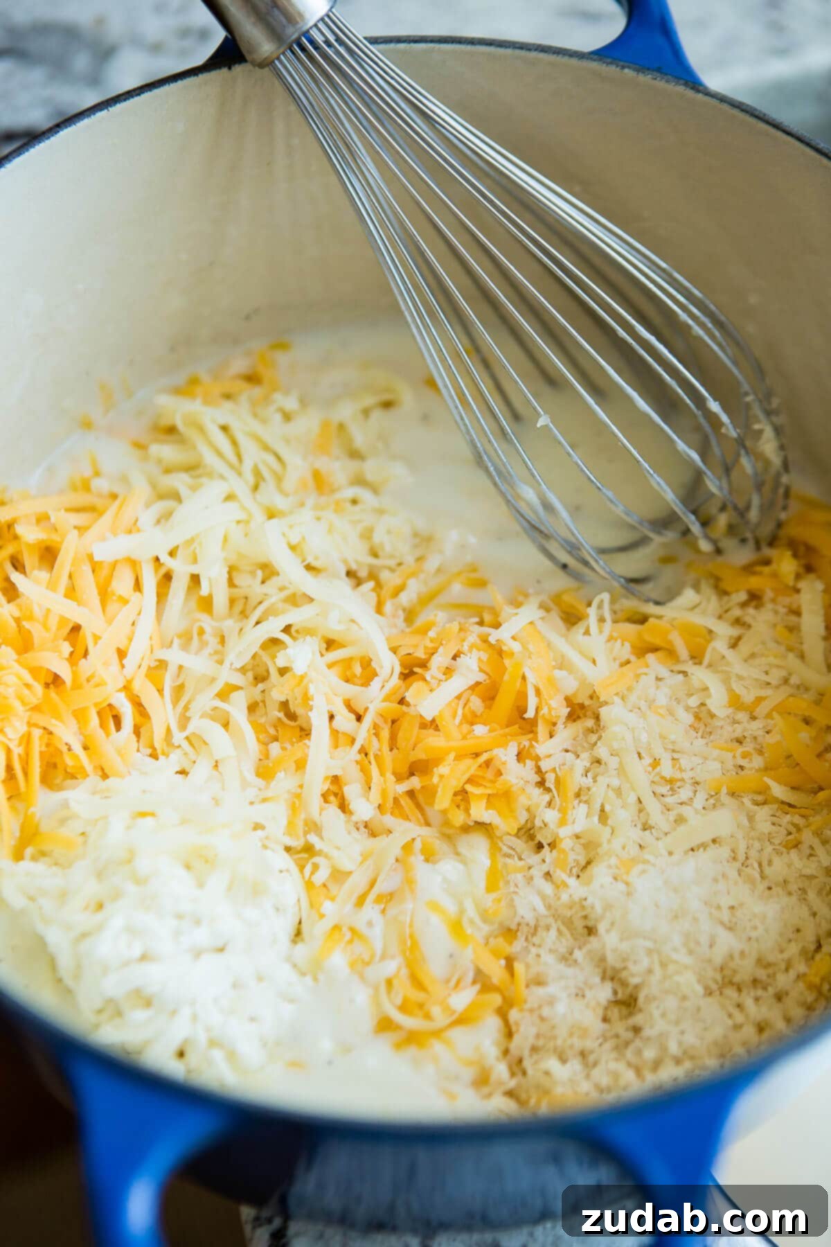 Loaded Chicken Bacon Ranch Mac and Cheese 3 three kinds of cheese and milk in a dutch oven with a whisk, illustrating the start of a rich, creamy cheese sauce