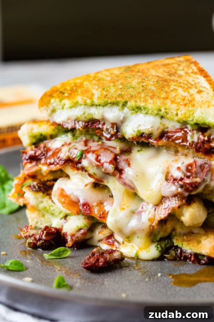 Two stacked sun dried tomato bacon pesto grilled cheese sandwiches with little basil leaves 