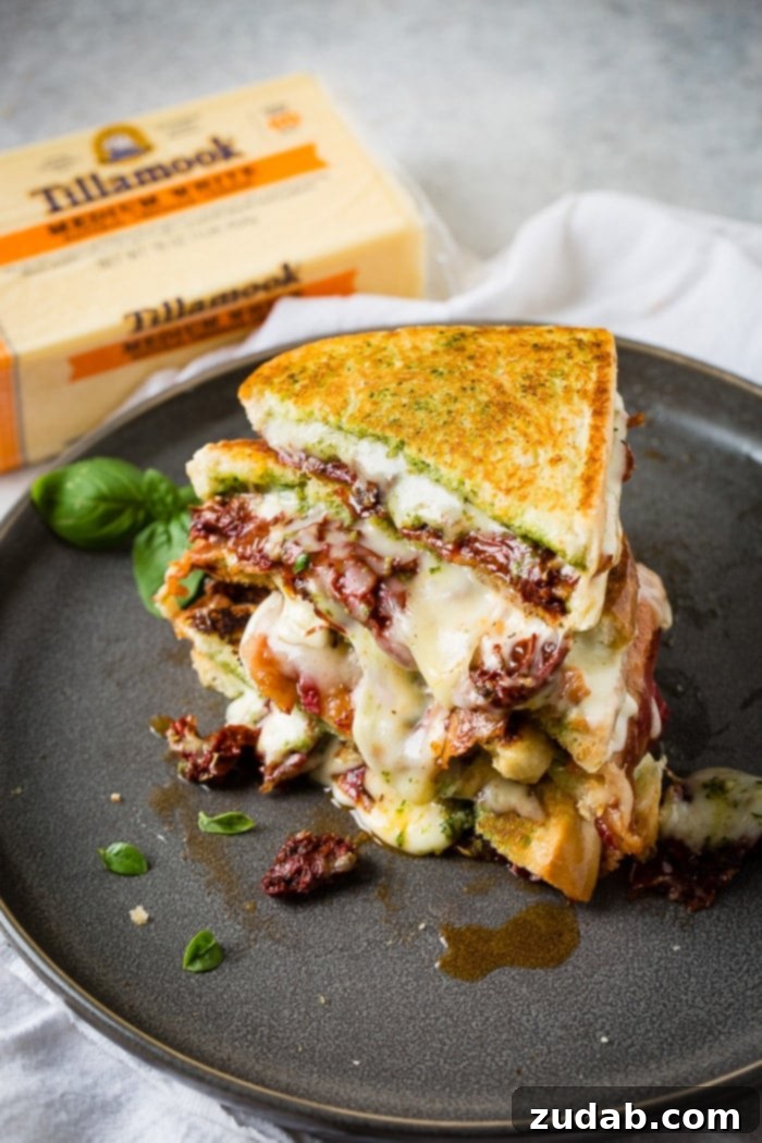 Two halves of a Sun Dried Tomato Bacon Pesto Grilled Cheese sandwich with basil garnish