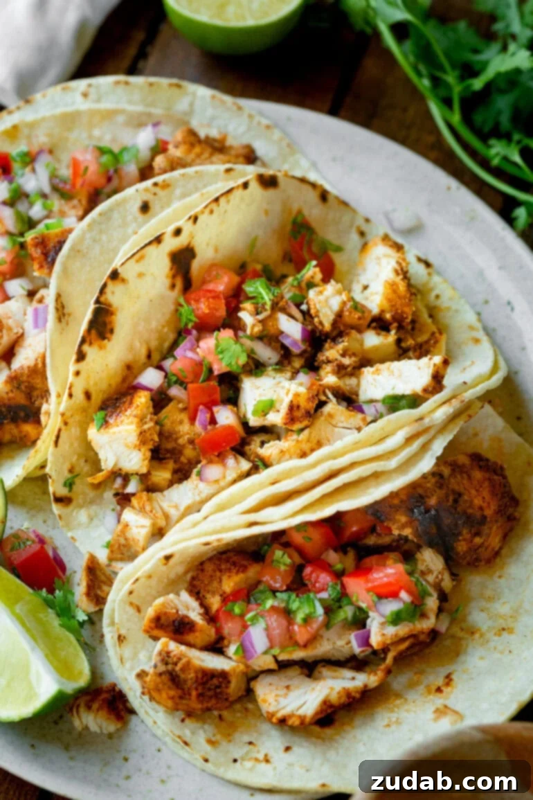 Quick and Delicious 30-Minute Grilled Chicken Tacos 7 A beautifully composed photo of three grilled chicken tacos, artfully arranged on a serving platter in soft corn tortillas and garnished with a generous topping of vibrant, homemade pico de gallo, ready to be enjoyed as a quick and easy meal.