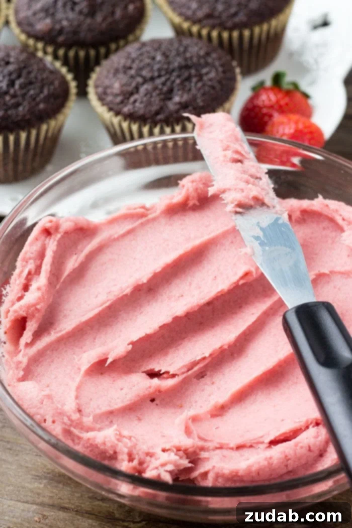Close-up of a chocolate cupcake generously frosted with luscious, pink strawberry buttercream, showcasing the perfect texture and vibrant color.