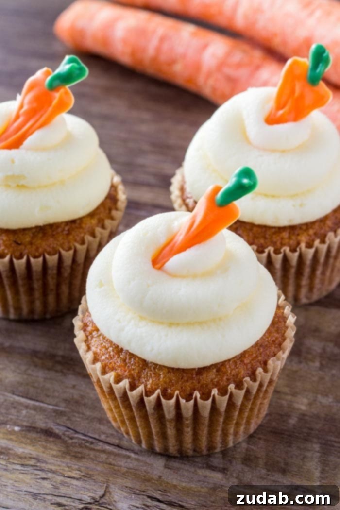 Moist Carrot Cake Cupcakes with Cream Cheese Frosting Three perfectly frosted carrot cake cupcakes with small candy carrots on top, arranged on a rustic wooden surface
